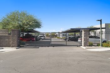The gate to the parking lot of a building with cars in it